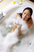 Woman having bubble bath, blowing soap suds - Asia Images Group