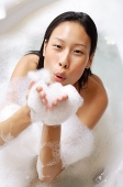 Woman in bathtub, blowing soap suds at camera - Asia Images Group