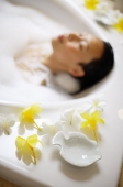 Woman in bathtub, focus on the flowers at the edge of tub - Asia Images Group