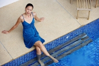 Young woman sitting by swimming pool, feet in water, looking at camera - Asia Images Group