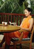 Woman sitting at table, reading a book - Asia Images Group