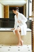 Woman in robe, sitting at edge of bath tub - Asia Images Group