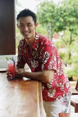 Man at beach bar, with drink, smiling at camera - Asia Images Group