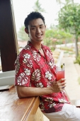 Man standing at bar counter, holding drink, smiling at camera - Asia Images Group