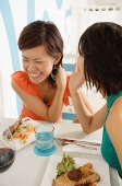 Young women in cafe, having lunch, one whispering to the other - Asia Images Group