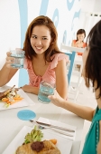 Young women in cafe, having lunch, holding glasses of water - Asia Images Group