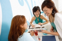 Young women talking over drinks in cafe, one woman mobile phone - Asia Images Group