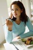 Young woman sitting at table, food in front of her, looking at camera - Asia Images Group