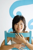 Young woman sitting on chair, smiling at camera - Asia Images Group
