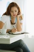 One woman sitting at table, writing - Asia Images Group