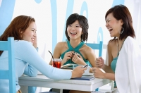 Three young women sitting in cafe, laughing - Asia Images Group