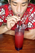 Man in floral shirt sipping drink through straw - Asia Images Group