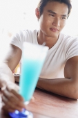 Man sitting at table, holding drink, selective focus - Asia Images Group