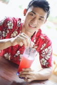 Man wearing floral shirt, holding a drink, looking at camera - Asia Images Group