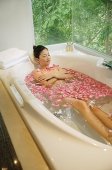 Woman taking a bath, flowers floating in water - Asia Images Group