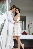 Couple standing in bedroom doorway, embracing - Asia Images Group