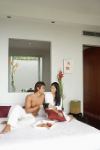 Couple sitting on bed, toasting with mugs - Asia Images Group