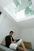 Man sitting at home, reading a book - Asia Images Group