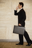 Businessman with briefcase, using mobile phone - Asia Images Group