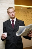 Businessman reading newspaper, holding paper cup - Asia Images Group