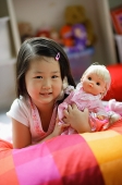 Girl lying on bed, holding a doll - Asia Images Group