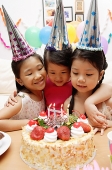 Three girls celebrating a birthday, looking at cake - Asia Images Group