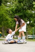 Children rollerblading, boy on the ground, girl pulling him up - Asia Images Group
