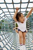 Young girl going through net tunnel in playground, other girls behind her - Asia Images Group