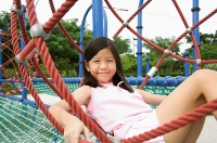 Girl sitting on jungle gym, smiling at camera - Asia Images Group