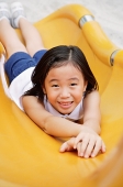 Girl on yellow slide, smiling at camera - Asia Images Group