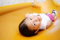 Girl lying on slide, smiling at camera - Asia Images Group
