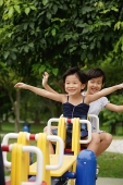 Two girls on a seesaw, arms outstretched - Asia Images Group
