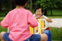 Two girls on a seesaw, one leaning on arms, smiling, eyes closed - Asia Images Group