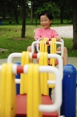 Young girl sitting on seesaw, smiling at camera - Asia Images Group