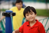 Boy in playground, looking at camera, people in the background - Asia Images Group