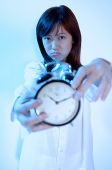 Young woman holding alarm clock, looking at camera, frowning - Asia Images Group