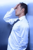 Man in shirt and tie, leaning on wall, hand on head - Asia Images Group