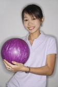 Woman holding purple bowling ball, smiling at camera - Asia Images Group
