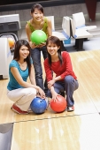 Three women in bowling alley, with bowling balls, smiling at camera - Asia Images Group