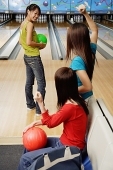 Women in bowling alley, one woman about to bowl, friends cheering her on - Asia Images Group