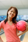 Woman at bowling alley holding bowling ball, hand on hip - Asia Images Group