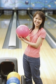 Woman at bowling alley holding bowling ball, smiling at camera - Asia Images Group