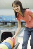 Woman at bowling alley selecting bowling ball, smiling at camera - Asia Images Group