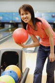 Woman at bowling alley with bowling ball, smiling at camera - Asia Images Group
