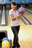 Woman at bowling alley holding bowling ball, smiling - Asia Images Group
