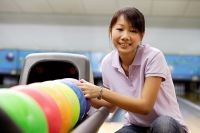 Woman selecting ball at bowling alley, smiling at camera - Asia Images Group