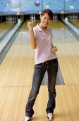 Woman standing at bowling alley, smiling, making a fist - Asia Images Group
