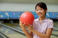 Woman at bowling alley, smiling, holding bowling ball - Asia Images Group