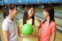 Women standing side by side at bowling alley, one woman holding green bowling ball - Asia Images Group