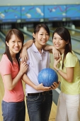 Three women at bowling alley, standing side by side, smiling at camera - Asia Images Group